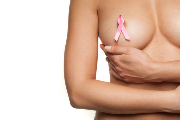 Naked woman wearing a pink breast cancer ribbon attached to her bare nipple as she cups her breast with her hand in a graceful movement, isolated on white