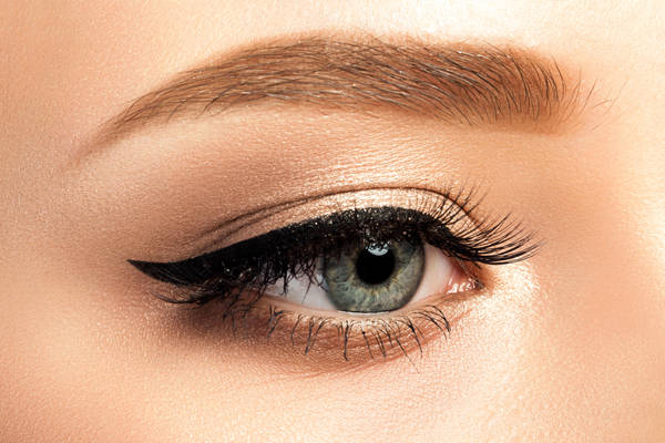 Close up view of gray woman eye with beautiful golden shades and black eyeliner makeup. Classic make up. Studio shot